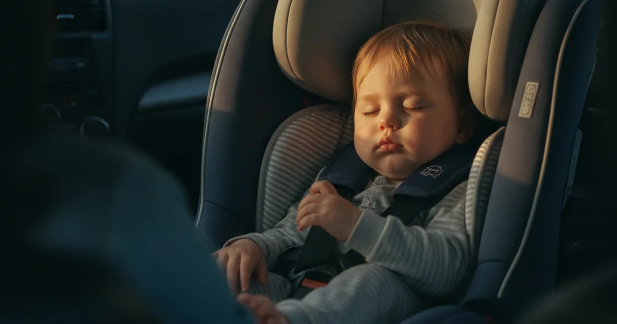 A toddler asleep in a rear-facing car seat, head tilted against the headrest, soft afternoon light through the car window